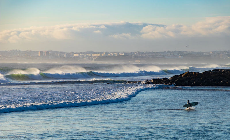 A surfer approaching Atlantic waves at Costa da Caparica, Portugal. Photo by Marc Winter via Pexels.